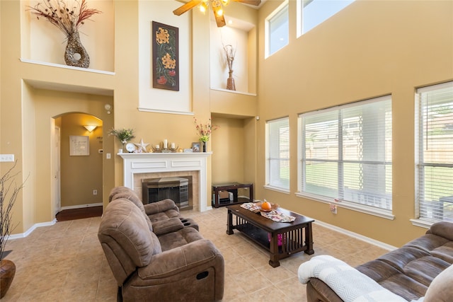 living room featuring a high ceiling, light tile patterned flooring, a tile fireplace, and ceiling fan