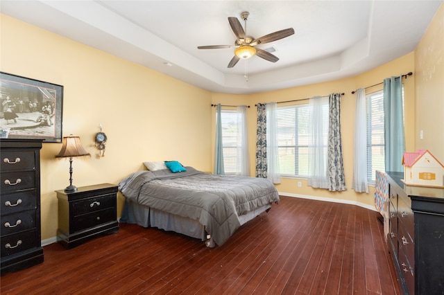 bedroom featuring dark wood-type flooring, ceiling fan, multiple windows, and a tray ceiling