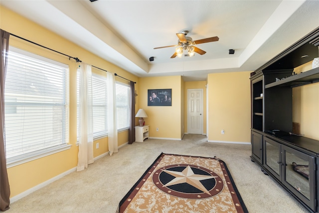 carpeted living room featuring a raised ceiling, ceiling fan, and plenty of natural light