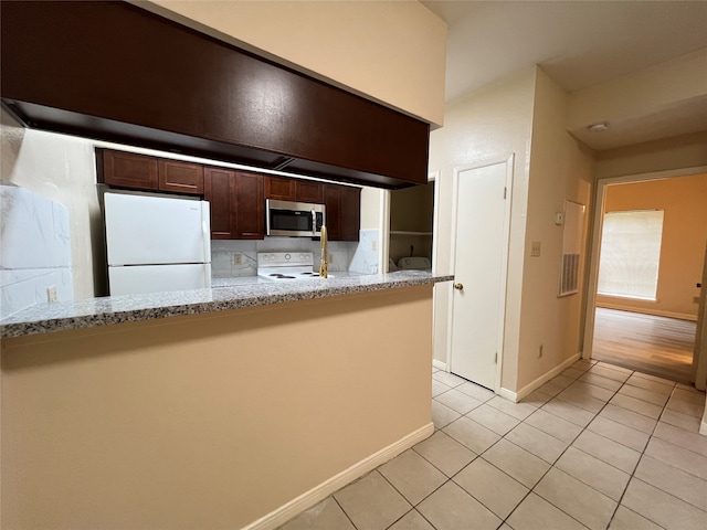 kitchen with kitchen peninsula, light stone countertops, light tile patterned floors, white appliances, and dark brown cabinets