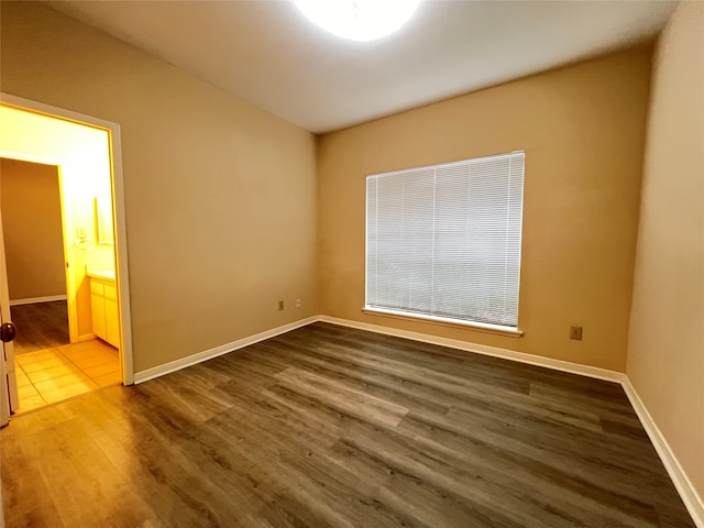 unfurnished bedroom featuring ensuite bathroom and hardwood / wood-style flooring