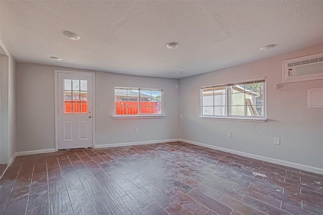 spare room with dark hardwood / wood-style floors, a textured ceiling, and an AC wall unit