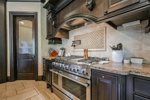 kitchen with double oven range, dark brown cabinets, decorative backsplash, and light stone counters