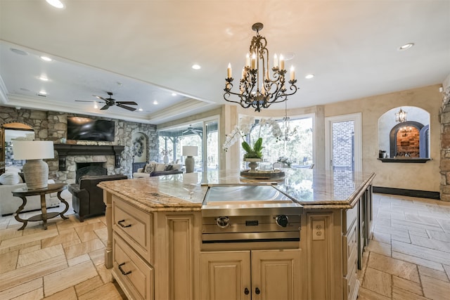 kitchen with light stone counters, ceiling fan with notable chandelier, a fireplace, hanging light fixtures, and a center island