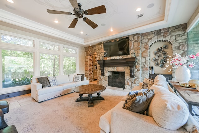 living room with ceiling fan, a stone fireplace, and ornamental molding