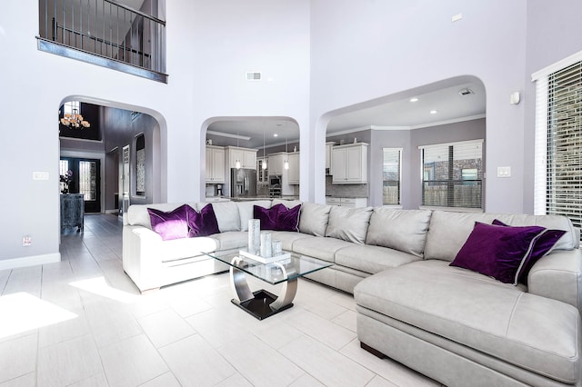 tiled living room featuring a towering ceiling, ornamental molding, and an inviting chandelier