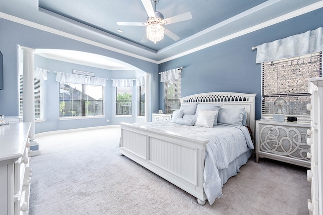 carpeted bedroom featuring decorative columns, a raised ceiling, ceiling fan, and crown molding