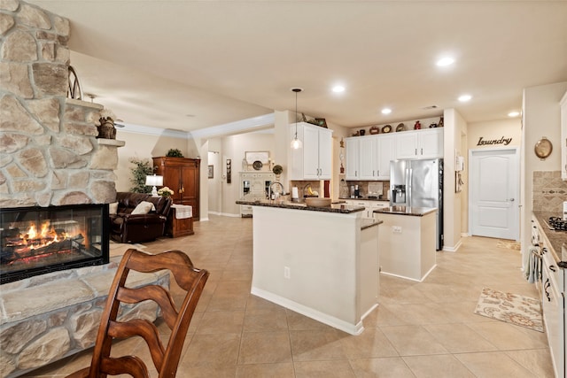 kitchen with white cabinetry, a fireplace, stainless steel fridge with ice dispenser, pendant lighting, and decorative backsplash