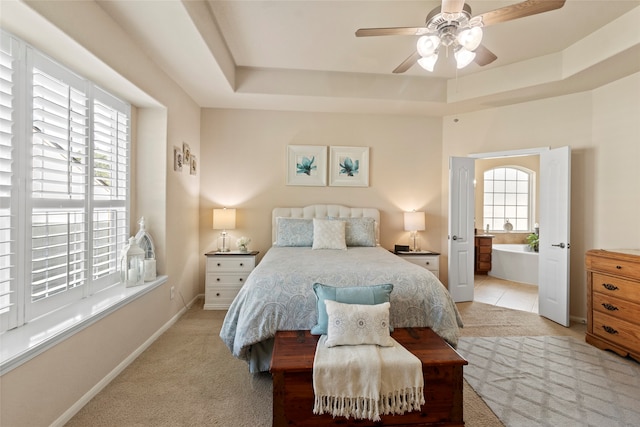 carpeted bedroom with ensuite bath, a raised ceiling, multiple windows, and ceiling fan