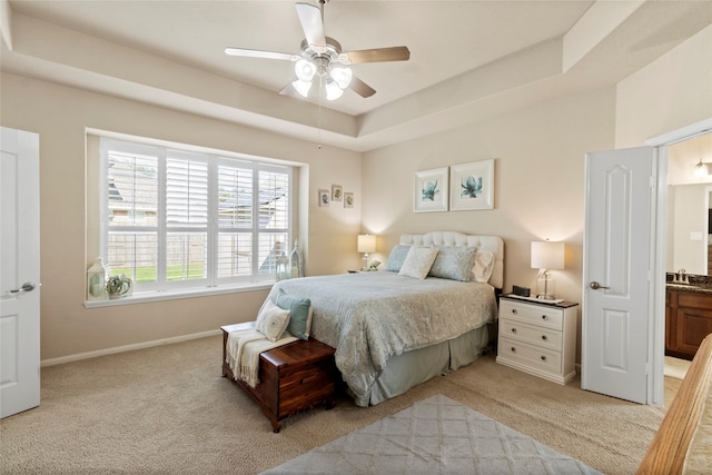 carpeted bedroom with ensuite bath, ceiling fan, sink, and a tray ceiling