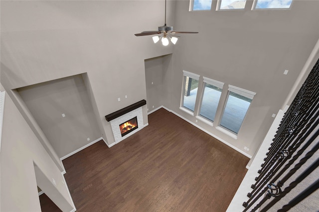 unfurnished living room featuring dark wood-type flooring, a high ceiling, a fireplace, and ceiling fan