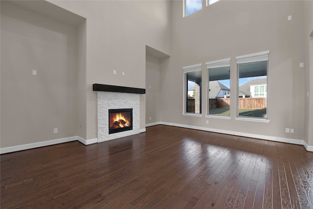 unfurnished living room with a wealth of natural light, a stone fireplace, a high ceiling, and dark hardwood / wood-style flooring