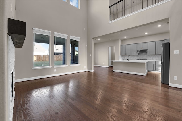 unfurnished living room with a towering ceiling, dark hardwood / wood-style floors, and sink