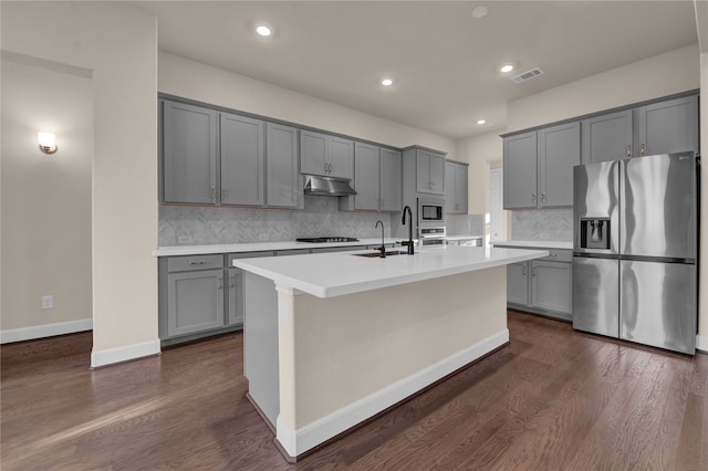 kitchen featuring gray cabinetry, backsplash, appliances with stainless steel finishes, dark hardwood / wood-style floors, and a kitchen island with sink