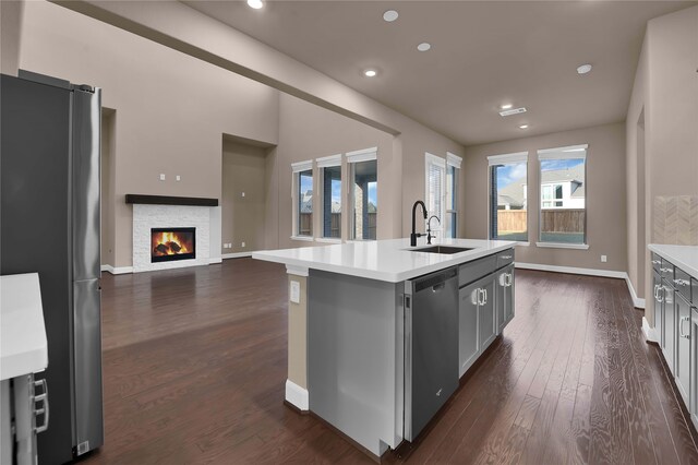 kitchen featuring sink, an island with sink, dark hardwood / wood-style floors, a fireplace, and appliances with stainless steel finishes