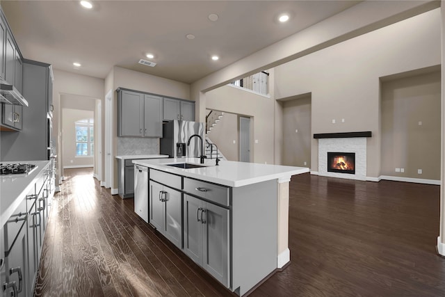 kitchen featuring dark hardwood / wood-style flooring, gray cabinetry, a center island with sink, and appliances with stainless steel finishes