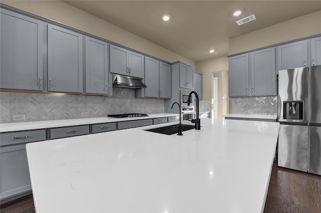 kitchen with dark wood-type flooring, sink, an island with sink, and stainless steel fridge