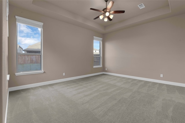 carpeted spare room featuring ceiling fan, a tray ceiling, and a healthy amount of sunlight