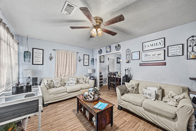 living room featuring ceiling fan, a textured ceiling, and light hardwood / wood-style floors