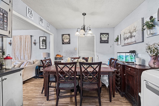 dining space featuring light hardwood / wood-style flooring, washer / clothes dryer, a textured ceiling, and an inviting chandelier