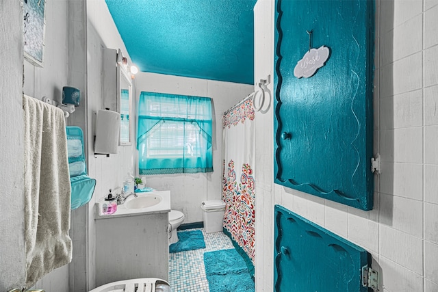 bathroom with vanity, a textured ceiling, toilet, and tile walls