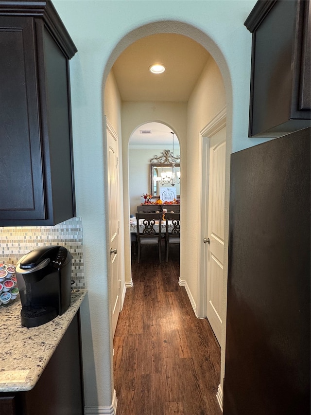 hallway with dark wood-type flooring and an inviting chandelier