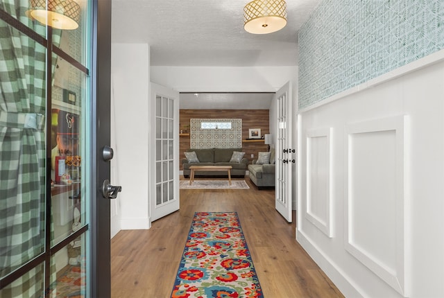 foyer entrance with a textured ceiling, french doors, wood walls, and hardwood / wood-style flooring