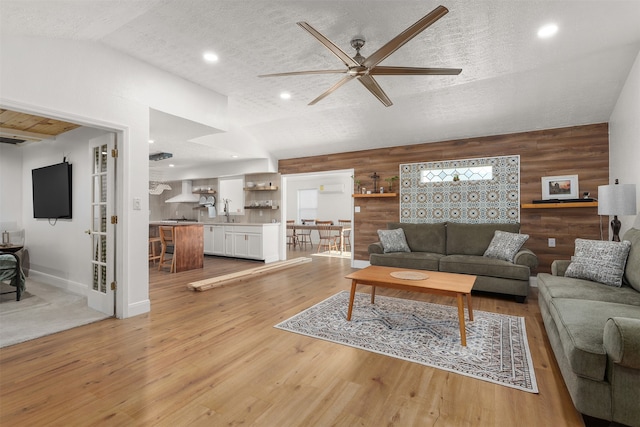 living room featuring wooden walls, a textured ceiling, vaulted ceiling, and light hardwood / wood-style flooring