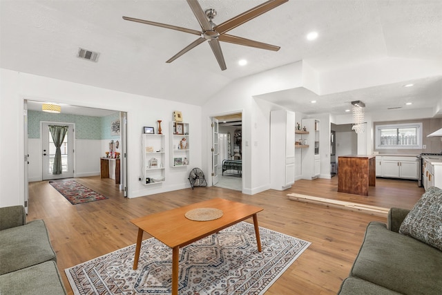 living room with a textured ceiling, light wood-type flooring, a healthy amount of sunlight, and vaulted ceiling