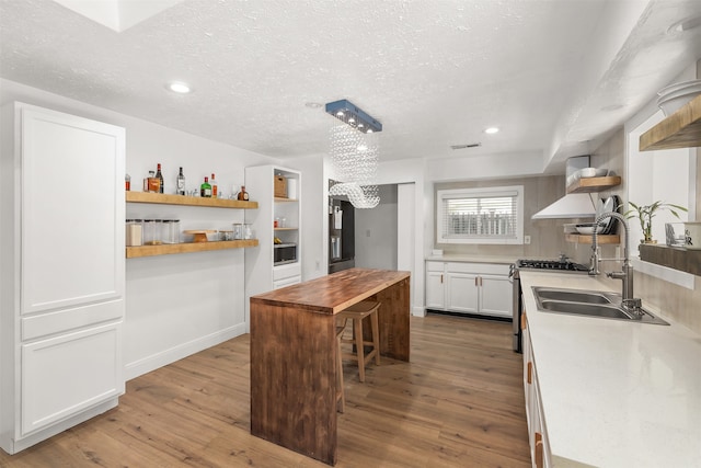 kitchen featuring wood-type flooring, stainless steel gas stove, white cabinetry, sink, and a center island