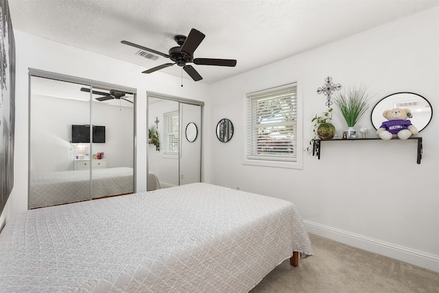 bedroom featuring a textured ceiling, carpet floors, ceiling fan, and two closets