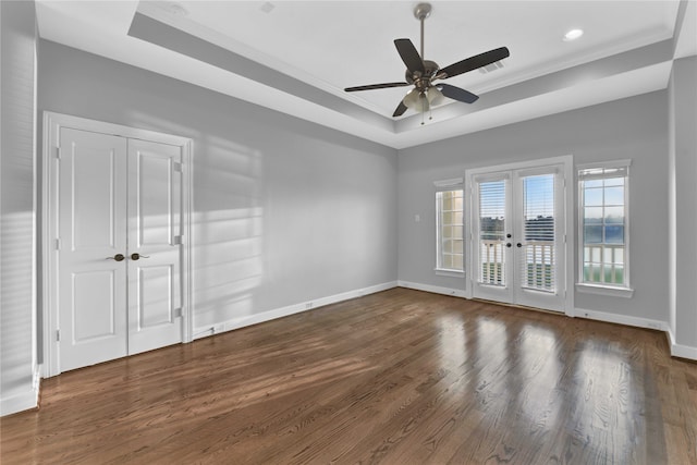 empty room with ceiling fan, a tray ceiling, crown molding, dark wood-type flooring, and french doors