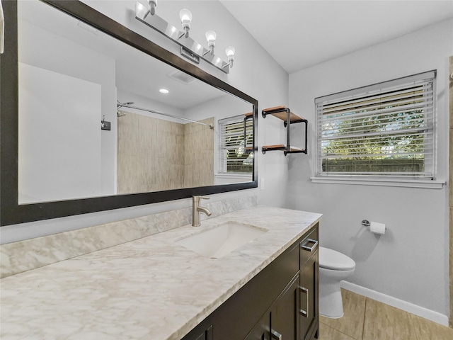 bathroom with a tile shower, a wealth of natural light, vanity, and toilet