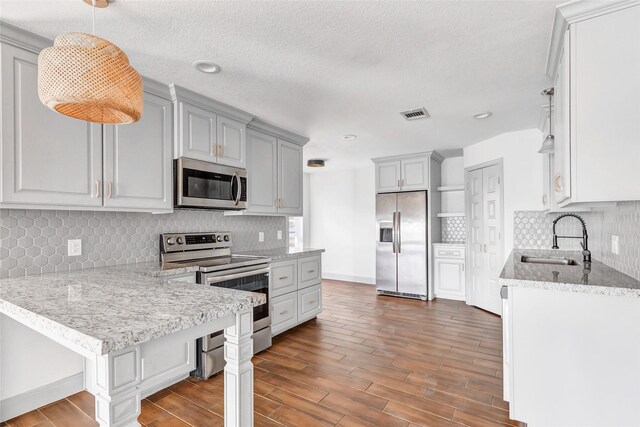 kitchen with light stone countertops, sink, hanging light fixtures, a textured ceiling, and appliances with stainless steel finishes