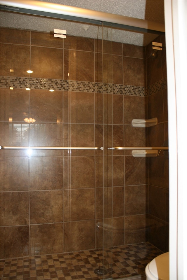 bathroom featuring a shower with shower door, a textured ceiling, and toilet