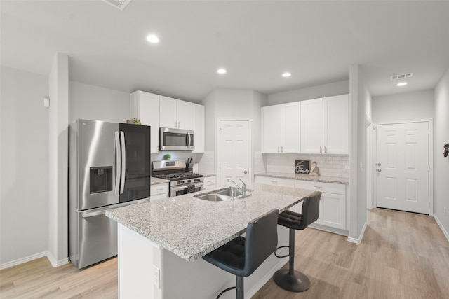 kitchen with stainless steel appliances, a center island with sink, a breakfast bar, and white cabinets