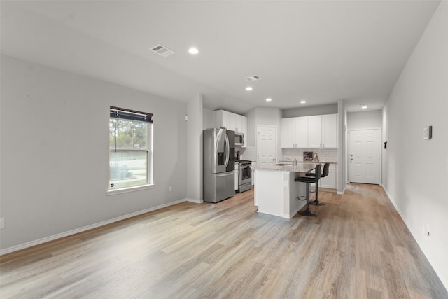 kitchen with stainless steel appliances, a center island with sink, white cabinetry, light stone countertops, and a kitchen bar