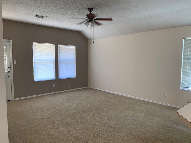 empty room featuring a textured ceiling, light colored carpet, lofted ceiling, and ceiling fan