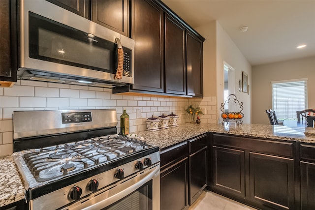 kitchen featuring light tile patterned floors, appliances with stainless steel finishes, dark brown cabinetry, light stone countertops, and decorative backsplash