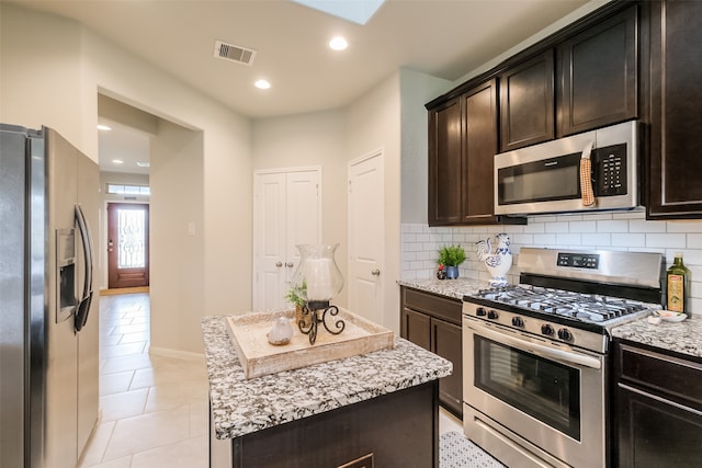 kitchen featuring light tile patterned flooring, dark brown cabinetry, tasteful backsplash, a kitchen island, and stainless steel appliances