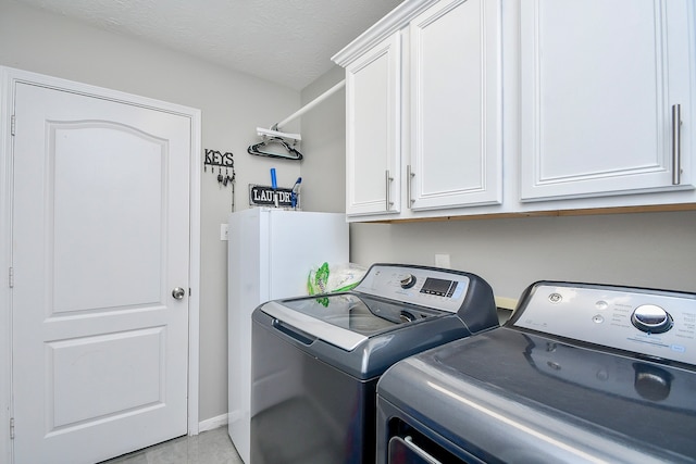 clothes washing area featuring cabinets, a textured ceiling, and washer and clothes dryer