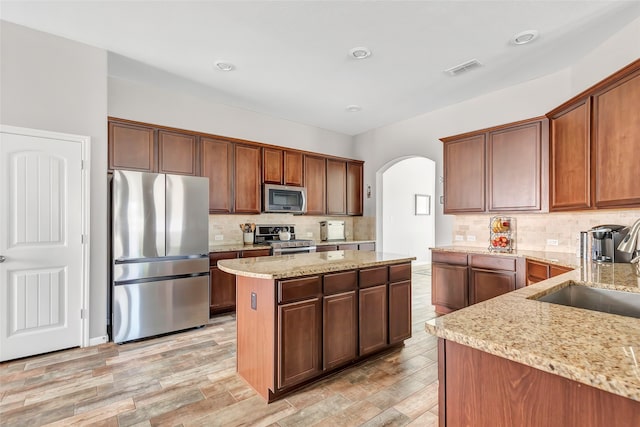 kitchen featuring light stone counters, backsplash, appliances with stainless steel finishes, light hardwood / wood-style floors, and a center island