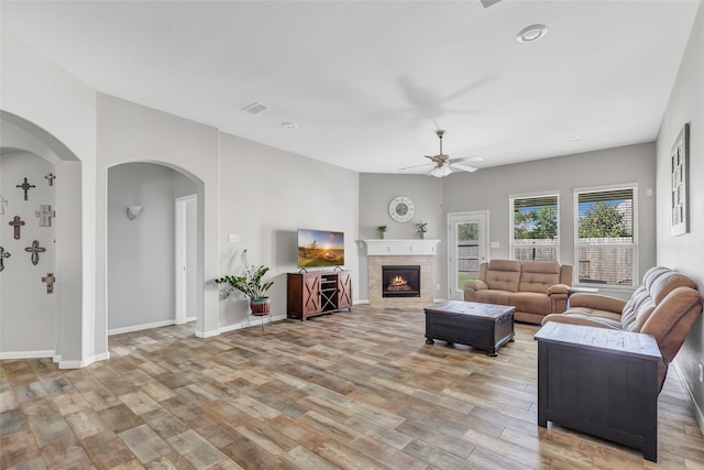 living room with ceiling fan, a tile fireplace, and light hardwood / wood-style flooring