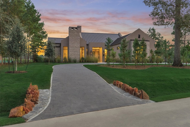 contemporary home featuring metal roof, a yard, decorative driveway, stucco siding, and a standing seam roof