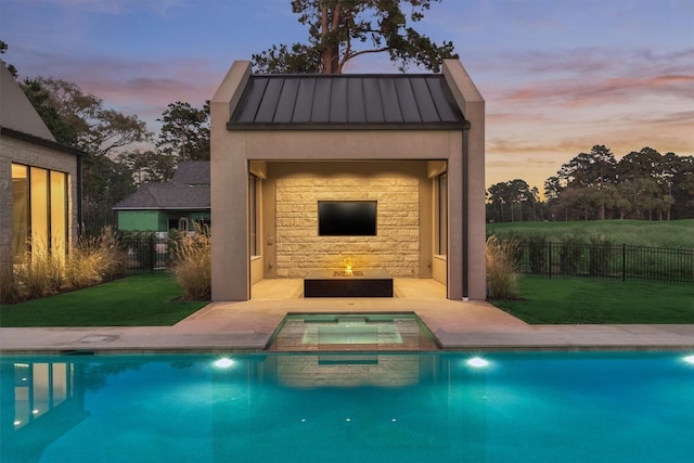 pool at dusk with a yard, a fire pit, and an in ground hot tub