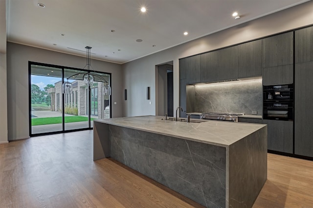 kitchen with pendant lighting, decorative backsplash, sink, an island with sink, and light hardwood / wood-style floors