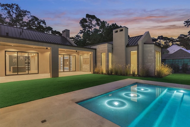 pool at dusk featuring a lawn and a patio