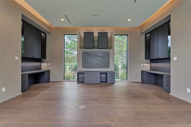 unfurnished living room featuring built in desk, light hardwood / wood-style flooring, and a wealth of natural light