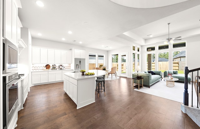 kitchen featuring a center island with sink, backsplash, dark hardwood / wood-style flooring, white cabinets, and oven