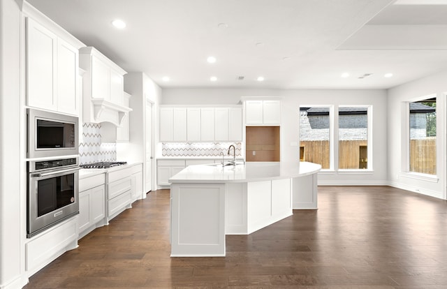 kitchen featuring stainless steel appliances, a center island with sink, white cabinets, dark wood-type flooring, and decorative backsplash